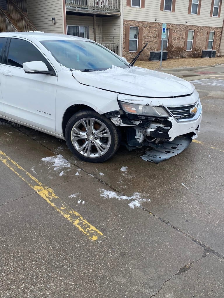 White Chevrolet Impala with severe damage to front left side parked on street near residential buildings