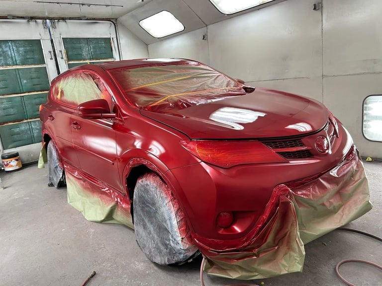 Red SUV covered with protective plastic sheeting in an auto body paint booth