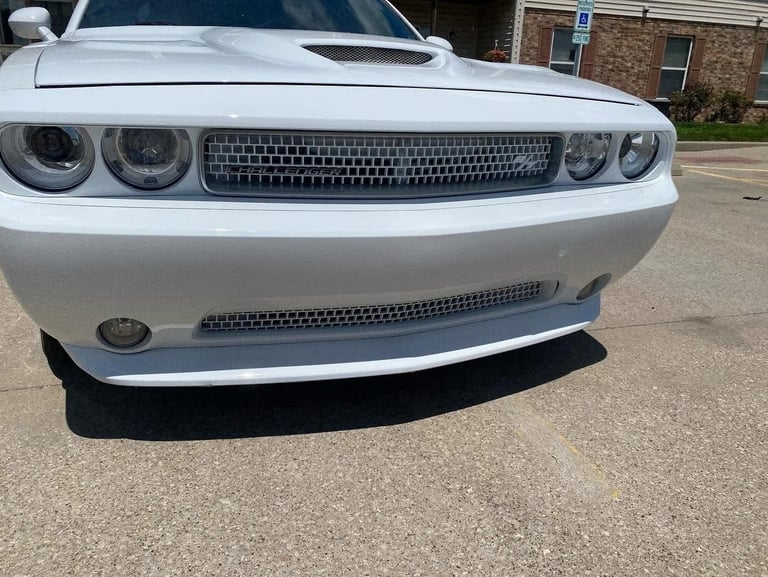 Front view of a white Dodge Challenger muscle car with dual headlights and chrome grille parked on a driveway