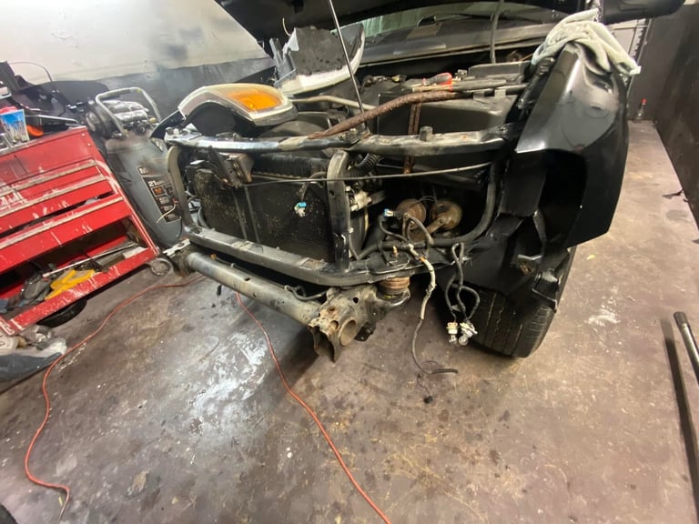 Disassembled car frame in a workshop showing stripped engine bay and exposed chassis components