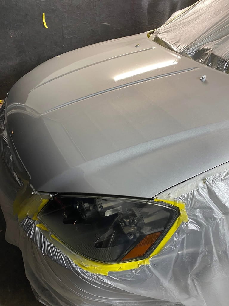 Silver car headlight being masked with yellow tape and plastic wrap during repair or painting preparation